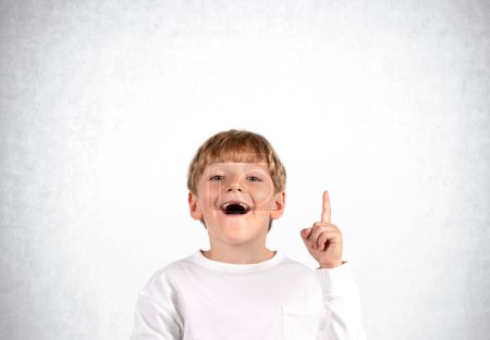 Téléchargez les photos : Écolier excité avec la bouche ouverte et le doigt pointant vers le haut, regard souriant heureux. Copier l'espace gris fond de mur en béton. Concept d'idée et plan - en image libre de droit