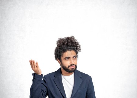 Foto de Hombre de negocios árabe con una mano en alto, retrato confuso y despistado. Copiar espacio fondo de pared de hormigón gris. Concepto de pregunta y solución - Imagen libre de derechos