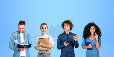 Foto de Retrato de grupo de cuatro estudiantes universitarios diversos hombres y mujeres con cuadernos y teléfonos inteligentes de pie sobre fondo azul. Concepto de trabajo en equipo, educación, amistad y lluvia de ideas - Imagen libre de derechos