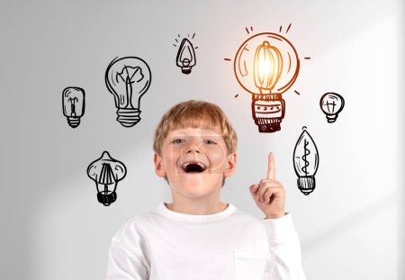 Photo for Happy school boy with opened mouth and finger pointing up, set of different lightbulbs doodle on white background. Concept of idea and inspiration - Royalty Free Image