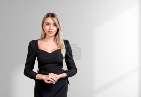 Téléchargez les photos : Attentif attrayant femme d'affaires portant tenue formelle tenant les mains ensemble près du mur blanc vide en arrière-plan. Concept de modèle, homme d'affaires prospère - en image libre de droit