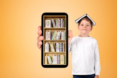 Foto de Niño sonriente mostrando teléfono inteligente con pantalla de teléfono grande con biblioteca digital sobre fondo naranja. Concepto de aplicación móvil y lectura - Imagen libre de derechos