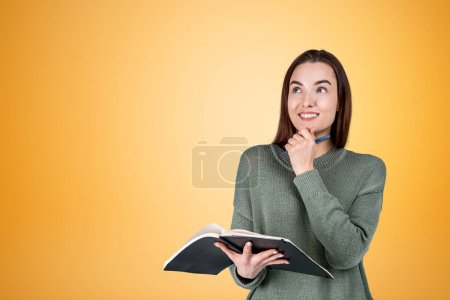Photo for Smiling inspired woman look up with notebook and hand to chin, copy space empty orange background. Concept of thoughts and idea - Royalty Free Image