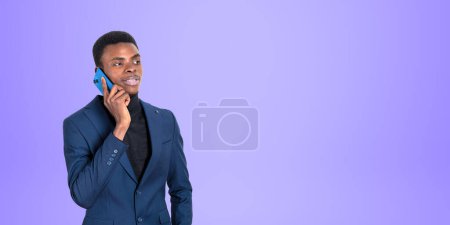 Téléchargez les photos : Portrait de jeune homme d'affaires afro-américain concentré en costume et col roulé parlant sur smartphone debout sur fond d'espace de copie violet. Concept de communication - en image libre de droit