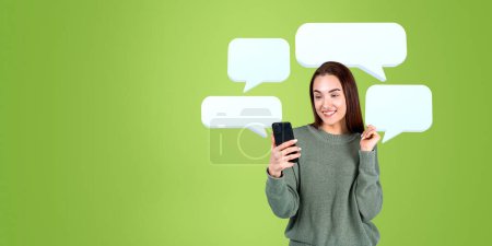 Photo for Portrait of smiling woman college student using smartphone over green background with blank speech bubbles. Concept of news, internet surfing and online communication in social media. Copy space - Royalty Free Image