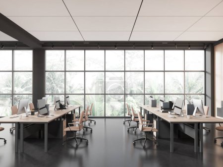 Foto de Interior coworking oscuro con sillones y ordenador PC en el escritorio en fila, piso de hormigón negro. Diseño moderno de la sala de trabajo con ventana panorámica en los trópicos. Renderizado 3D - Imagen libre de derechos