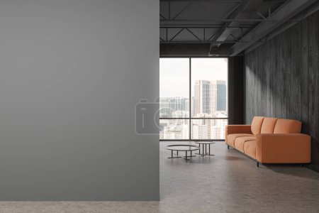 Foto de Interior oscuro de negocios con sofá naranja y mesa de centro, suelo de hormigón gris. Minimalista espacio de relax en el loft de oficinas con ventana panorámica en Kuala Lumpur. Simular la partición de espacio de copia. Renderizado 3D - Imagen libre de derechos