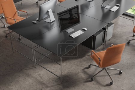 Foto de Vista superior del interior de coworking con ordenadores PC en escritorio negro, sillones marrones en fila en piso de hormigón gris. Lugar de trabajo minimalista con tecnología y ventana. Renderizado 3D - Imagen libre de derechos
