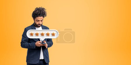 Photo for Concentrated arab businessman typing in phone, five stars rating and empty copy space orange background. Good review from customer and positive feedback. Concept of online service - Royalty Free Image