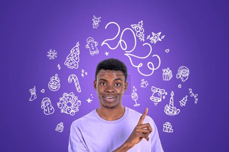 Téléchargez les photos : Heureux doigt d'homme noir pointant vers doodle avec 2023 année, accessoires et décoration. Bonhomme de neige, Père Noël claus et cadeaux sur fond violet. Concept de célébration - en image libre de droit