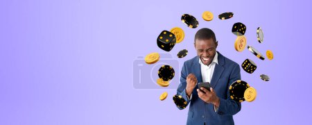Téléchargez les photos : Homme d'affaires africain avec bras levé et smartphone, dés tombants et jetons de poker avec des pièces sur l'espace de copie fond violet vide. Concept de pari en ligne, victoire et chance - en image libre de droit