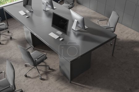 Foto de Vista superior del interior de coworking con ordenadores PC en escritorio compartido, sillones en fila en piso de hormigón gris. Lugar de trabajo minimalista con tecnología y taquillas, ventana. Renderizado 3D - Imagen libre de derechos