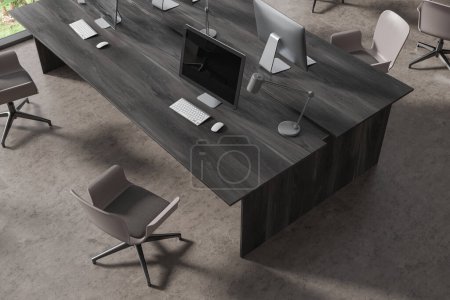 Foto de Vista superior del interior de coworking con ordenadores PC en escritorio de madera negro, sillas en fila en piso de hormigón gris. Elegante espacio de trabajo con muebles minimalistas para el trabajo en equipo. Renderizado 3D - Imagen libre de derechos