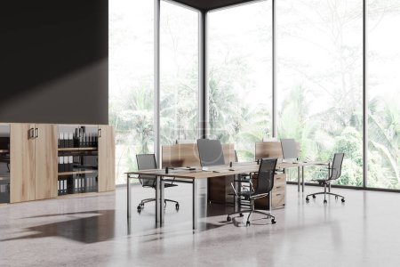 Foto de Interior de oficina moderno oscuro con sillones y monitores de pc en la mesa, vista lateral piso de hormigón ligero. Esquina minimalista de coworking con aparador y ventana panorámica en trópicos. Renderizado 3D - Imagen libre de derechos