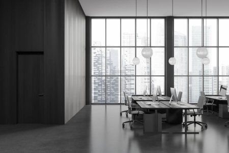 Foto de Interior de elegante oficina de espacio abierto con paredes de madera gris y oscura, piso de hormigón, fila de mesas de ordenador con sillas grises y puerta en pared de madera oscura. renderizado 3d - Imagen libre de derechos
