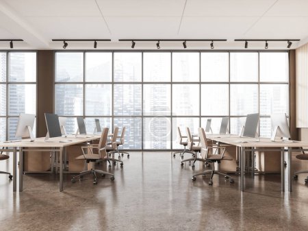 Foto de Interior de la moderna oficina de espacio abierto con paredes de color beige y marrón, suelo de hormigón, mesas de ordenador masivas con sillas marrones de pie cerca de ventanas panorámicas con paisaje urbano. renderizado 3d - Imagen libre de derechos