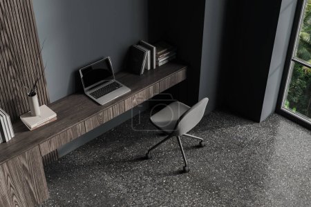 Foto de Vista superior del elegante interior de la oficina en casa con paredes grises y de madera, piso de hormigón, cómodo escritorio con computadora portátil de pie en él y silla gris. renderizado 3d - Imagen libre de derechos