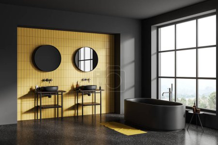 Téléchargez les photos : Intérieur de la salle de bain élégante avec des murs carrelés gris et jaune, sol en béton, confortable baignoire grise debout près de la fenêtre et confortable double lavabo avec deux miroirs ronds. Rendu 3d - en image libre de droit