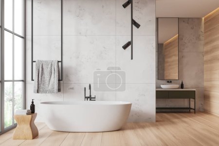 Photo for Interior of modern bathroom with white marble and wooden walls, wooden floor, comfortable white bathtub standing near window and cozy sink with vertical mirror in background. 3d rendering - Royalty Free Image