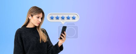 Photo for Concentrated young woman looking at the phone in hand, five stars rating and empty copy space granite background. Good review from customer and positive feedback. Concept of online service - Royalty Free Image