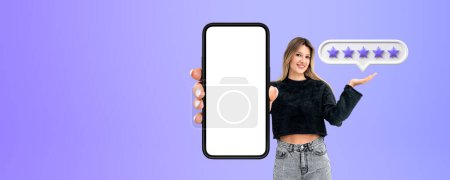 Photo for Smiling young woman hand showing a mockup phone screen, purple background. Giving five stars, high rating and share her positive experience. Concept of online business and client feedback - Royalty Free Image
