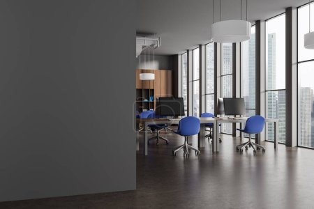 Foto de Esquina de la moderna oficina de espacio abierto con paredes grises, suelo de piedra, fila de escritorios de ordenador con sillas azules, librería de madera con carpetas y pared de espacio de copia a la izquierda. renderizado 3d - Imagen libre de derechos