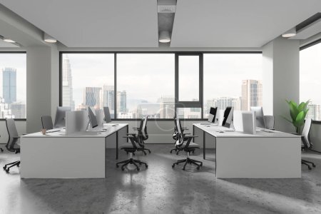 Foto de Interior de coworking blanco con sillones y ordenadores PC en escritorio compartido, suelo de hormigón gris. Acogedor lugar de trabajo con muebles en fila, ventana panorámica en Kuala Lumpur vista a la ciudad. Renderizado 3D - Imagen libre de derechos