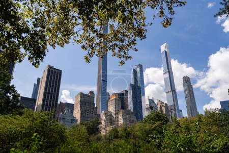 Téléchargez les photos : Des gratte-ciels de New York, des arbres verts à Central Park sous un ciel nuageux. Bâtiments de centre-ville, mégapole et centre de commerce financier. Manhattan et paysage urbain d'affaires - en image libre de droit