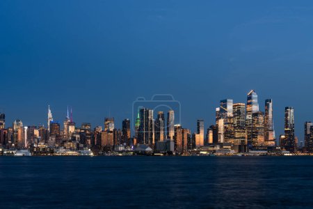 Foto de Rascacielos de Nueva York y paseo marítimo del río Hudson por la noche, vista panorámica de edificios de oficinas con luces, paisaje urbano del centro financiero corporativo. Manhattan lado oeste horizonte y río - Imagen libre de derechos