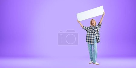 Téléchargez les photos : Femme souriante debout sur toute la longueur, montrant un panneau blanc maquette dans les mains sur fond violet vide. Concept de recommandation, d'annonce et de signature - en image libre de droit