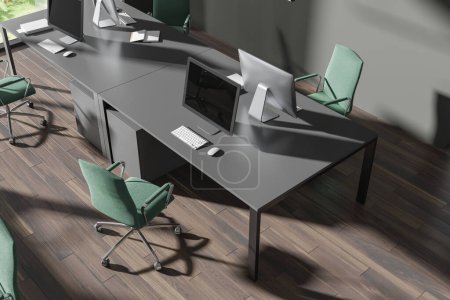 Foto de Vista superior del interior oscuro coworking con escritorio pc en mesa compartida, piso de madera dura. Elegante rincón de trabajo con sillones verdes en fila y tecnología. Renderizado 3D - Imagen libre de derechos