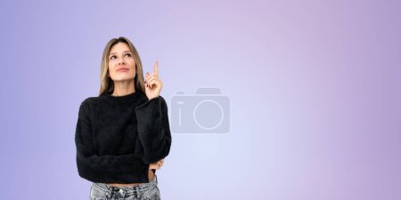 Foto de Mujer joven pensativa y soñadora en traje casual, dedo índice apuntan hacia arriba en el espacio de copia vacío fondo púrpura. Concepto de puesta en marcha, idea y plan de negocio - Imagen libre de derechos