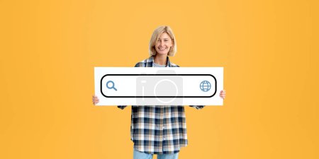 Foto de Mujer rubia sonriente mostrando letrero con maqueta de barra de búsqueda en blanco, fondo naranja. Información navegar por Internet. Concepto de búsqueda en línea, sitio web y solicitud - Imagen libre de derechos