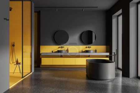 Téléchargez les photos : Intérieur de la salle de bain élégante avec des murs carrelés gris et jaune, sol en béton, confortable baignoire grise debout près des fenêtres, porte vitrée douche et double lavabo avec des miroirs ronds. Rendu 3d - en image libre de droit