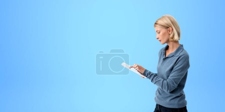 Photo for Portrait of concentrated young woman wearing casual clothes and using tablet computer standing over blue copy space background. Concept of technology and education - Royalty Free Image