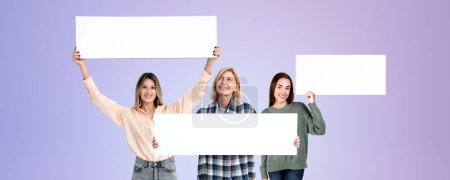 Photo for Happy three young women holding up mockup blank signboards in hands, wide format purple background. Concept of advertisement, announcement, sale, marketing and offer - Royalty Free Image