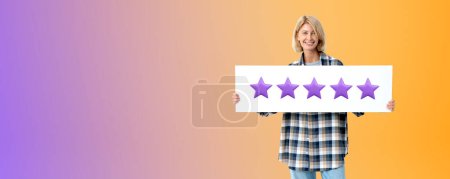 Photo for Portrait of happy young woman in casual clothes holding five star sign standing over purple copy space background. Concept of product and service evaluation and client feedback - Royalty Free Image