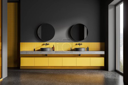 Foto de Interior del baño del hotel oscuro y amarillo con doble lavabo y espejo redondo, accesorios y suelo de granito gris. Ventana panorámica en el campo. Renderizado 3D - Imagen libre de derechos