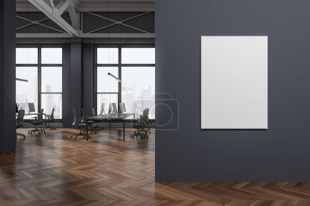Foto de Interior de acogedora oficina de espacio abierto de estilo industrial con paredes grises, suelo de madera, fila de escritorios de computadora con sillas grises y póster de maqueta vertical a la derecha. renderizado 3d - Imagen libre de derechos