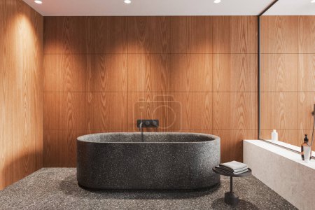 Foto de Moderno cuarto de baño de madera interior con bañera y accesorios, estante de piedra con gel de baño y mesa auxiliar con toalla. Tabique de vidrio y suelo de granito gris. Renderizado 3D - Imagen libre de derechos