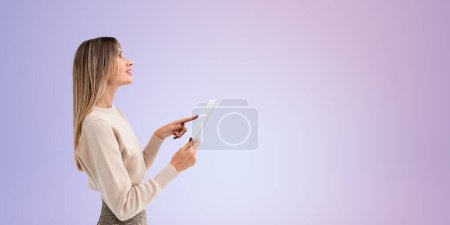 Foto de Sonriente joven mujer dedo toque tableta y mirar hacia arriba, perfil de retrato sobre fondo púrpura vacío. Comunicación digital y redes sociales. Concepto de red empresarial y compras en línea - Imagen libre de derechos
