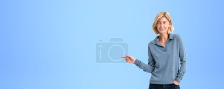 Photo for Portrait of cheerful young European woman pointing sideways standing over blue copy space background. Concept of product and service advertising - Royalty Free Image