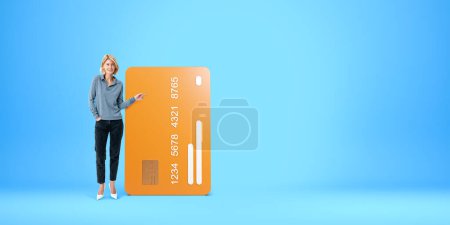 Téléchargez les photos : Femme blonde souriante doigt pleine longueur pointant vers une grande maquette de carte de crédit. Concept de recommandation, paiement, achat, finance et monnaie électronique - en image libre de droit
