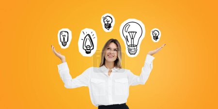 Photo for Smiling and dreaming young woman portrait with open hand palms, light bulbs doodle drawing on orange background. Concept of brainstorm, creativity and new idea - Royalty Free Image