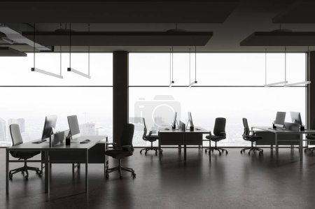 Foto de Interior coworking oscuro con escritorio pc en la mesa de trabajo en fila, piso de hormigón gris. Espacio de trabajo minimalista con ventana panorámica sobre los rascacielos de París. Renderizado 3D - Imagen libre de derechos