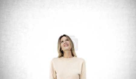 Photo for Thoughtful smiling young woman looking up, dreaming portrait on copy space empty grey concrete wall background. Concept of idea, plan, thoughts and decision - Royalty Free Image