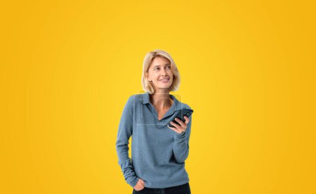 Foto de Dreaming smiling woman portrait using phone, empty copy space yellow background. Concept of online network, device, internet communication and social media - Imagen libre de derechos