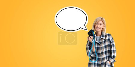 Téléchargez les photos : Smiling woman with a camera in hand, photographer with mock up blank cloud thought bubble on orange background. Concept of idea, creativity and inspiration - en image libre de droit