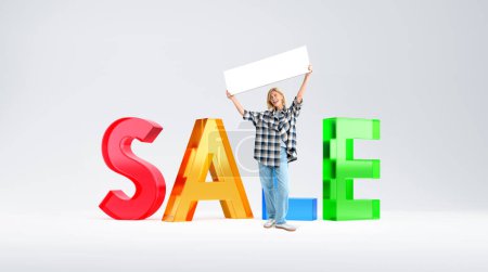 Téléchargez les photos : Young woman with mock up signboard standing near colorful sale sign over white background. Concept of discount and holiday season - en image libre de droit
