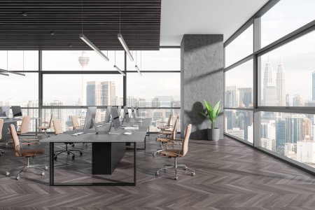 Foto de Dark coworking interior with pc desktop on table in row, hardwood floor. Stylish workplace with panoramic window on Kuala Lumpur skyscrapers. 3D rendering - Imagen libre de derechos